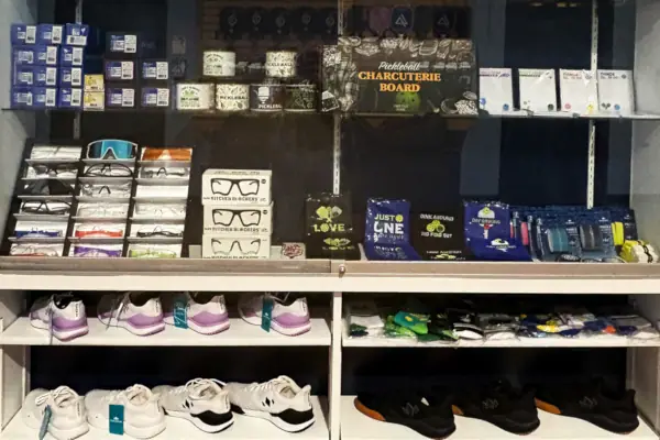 Display case featuring pickleball accessories, including eyewear, towels, & socks, alongside various athletic shoes.